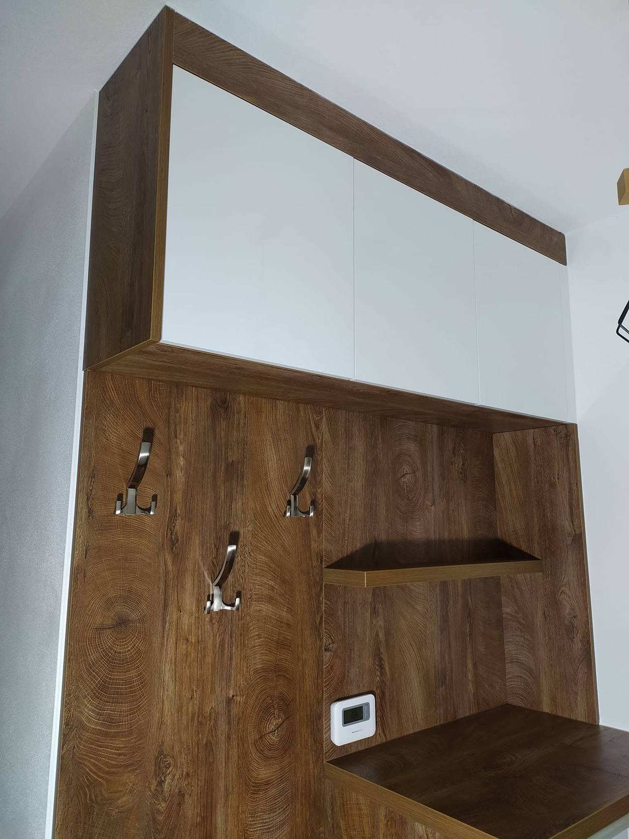 Biele horné skrinky nad tmavým panelom s háčikmi