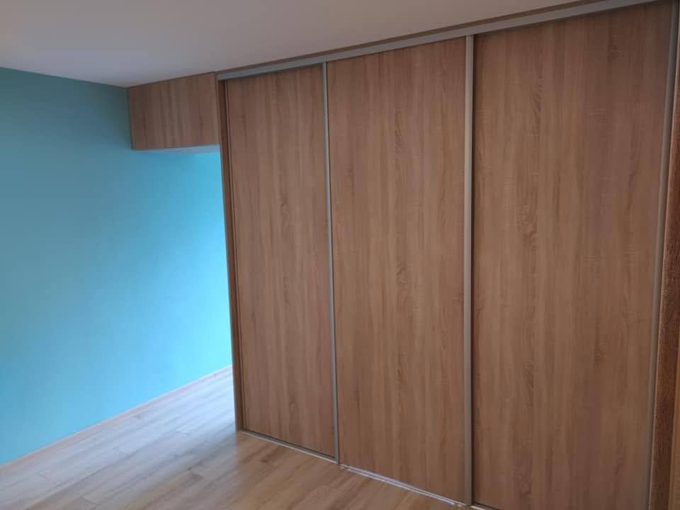 Dreitüriger Eichendekor-Schrank in Nische neben türkiser Wand