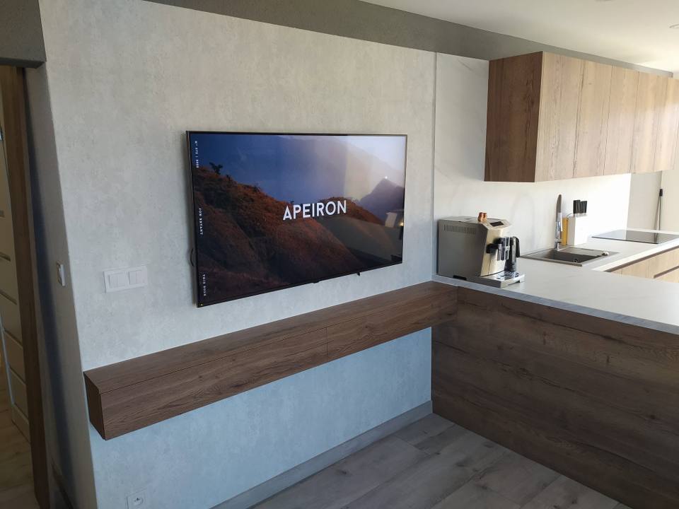 Wohnzimmer-TV-Wand in Betonoptik mit schwebendem Nussbaumbord über der Kochinsel