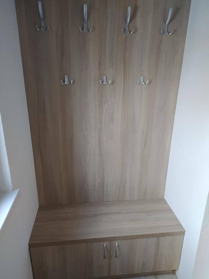 Garderobenpaneel mit vier Haken über einer Sitzbank mit zwei griffosen Laden.