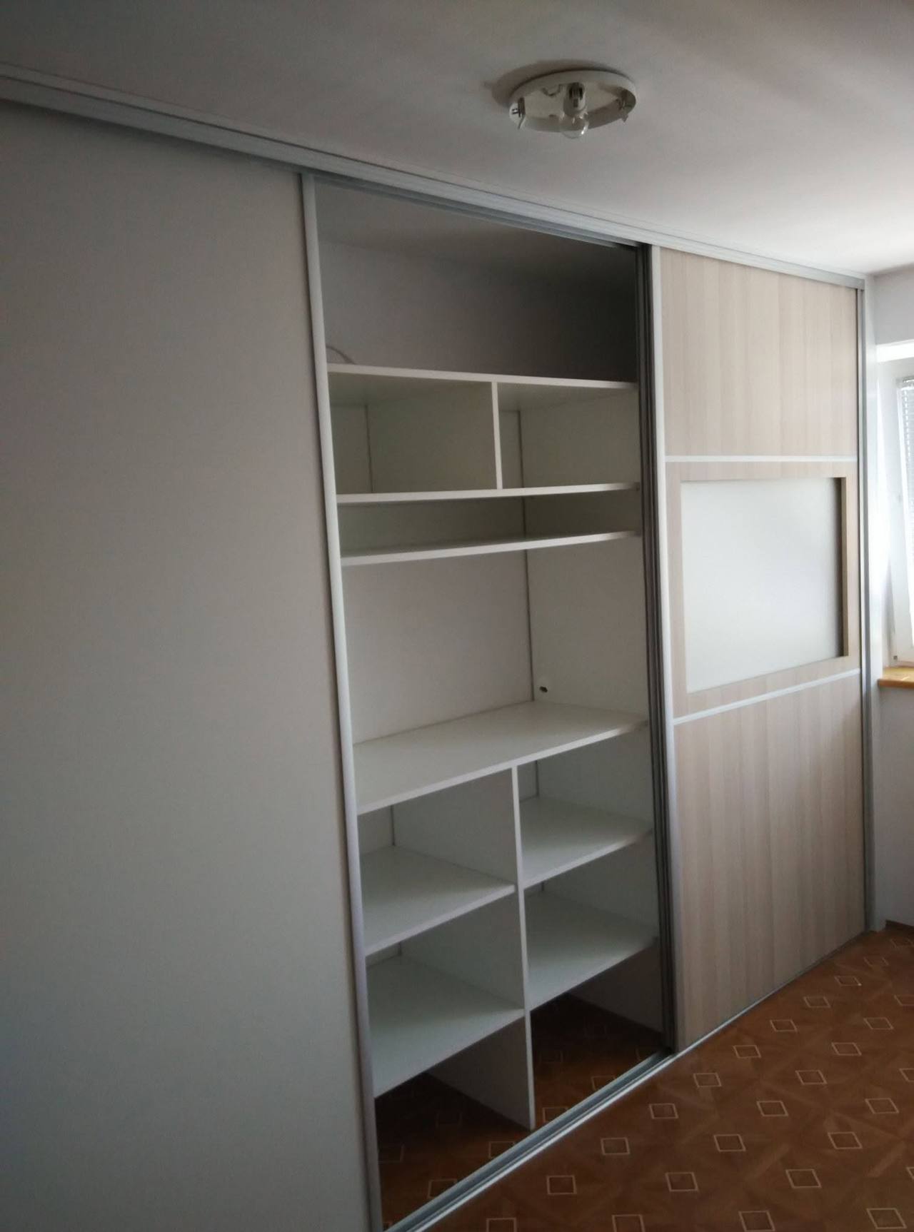 Otvorená posuvná skriňa s bielymi policami za sivými dverami
