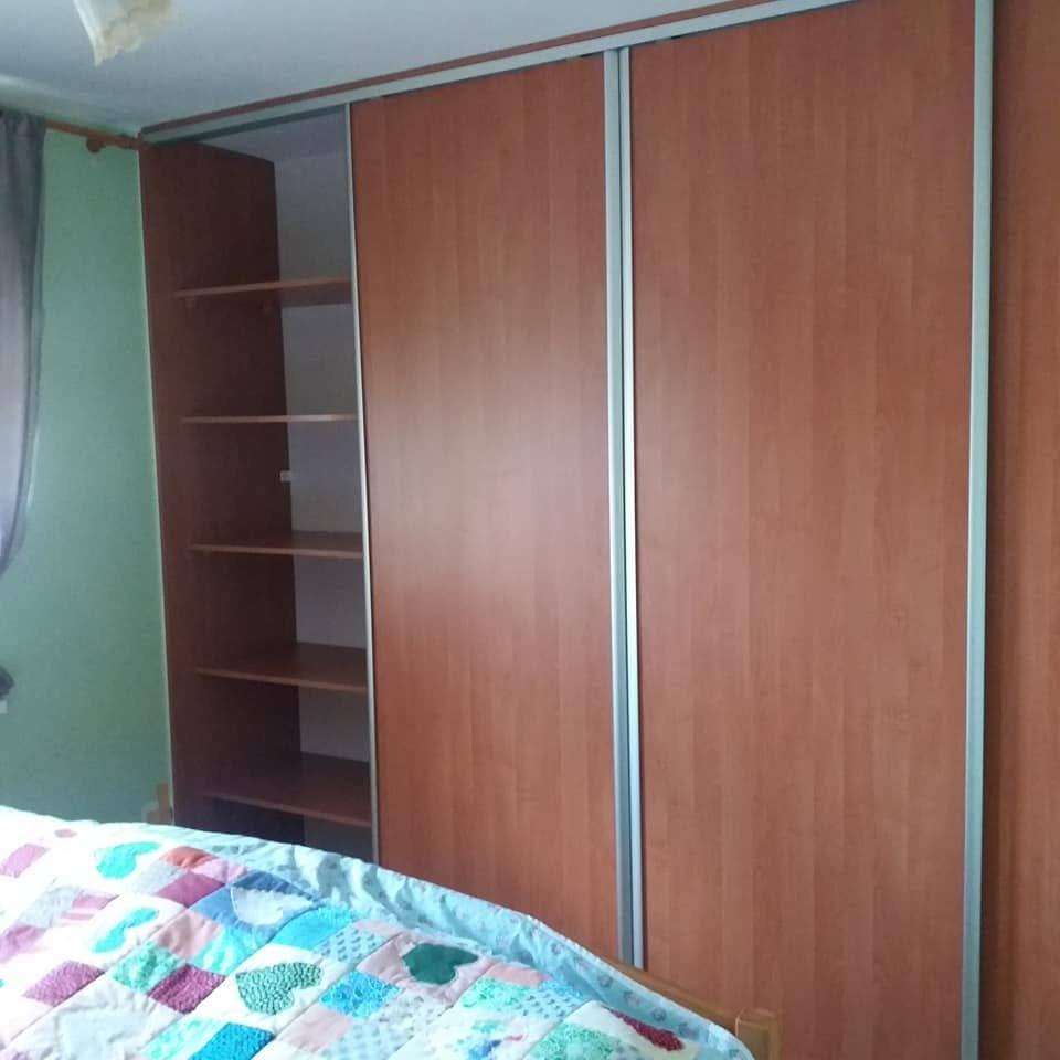 Geöffnete Kastentür mit dichten Böden über dem Bett mit türkisfarbener Decke.