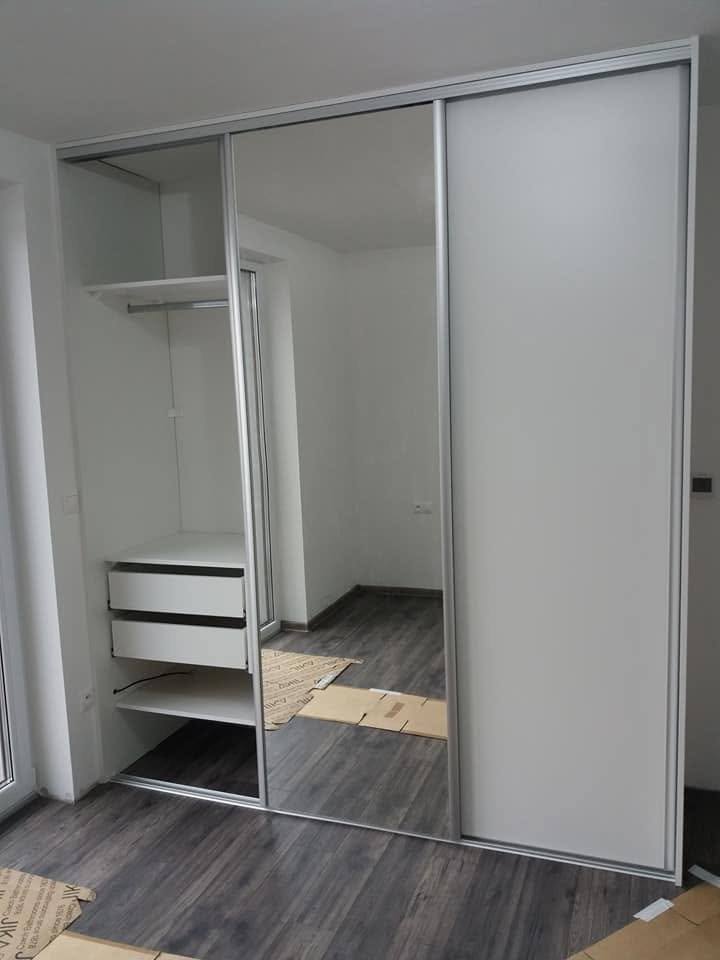 Otvorená biela skriňa so zásuvkami a šatnou tyčou vedľa zrkadla.