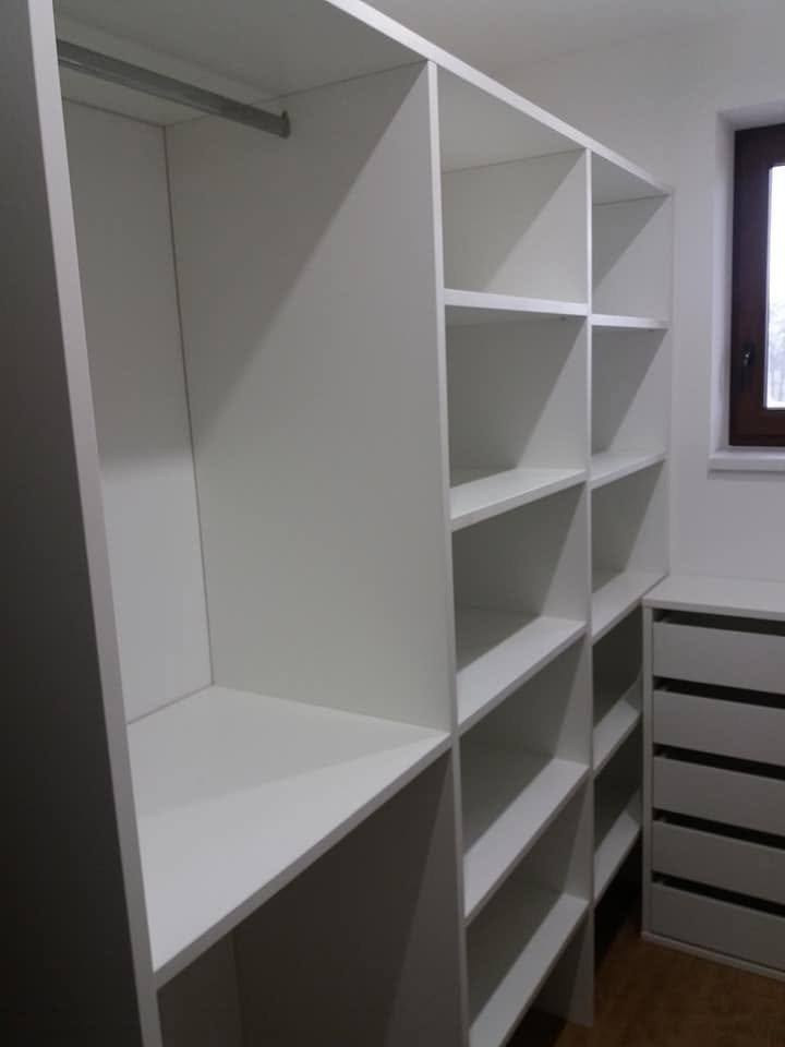 Begehbarer Kleiderkasten mit weißen Böden am Eckfenster.