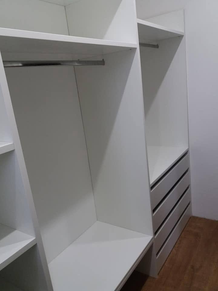 Kleiderstange und graue Laden im weißen Einbaukasten.
