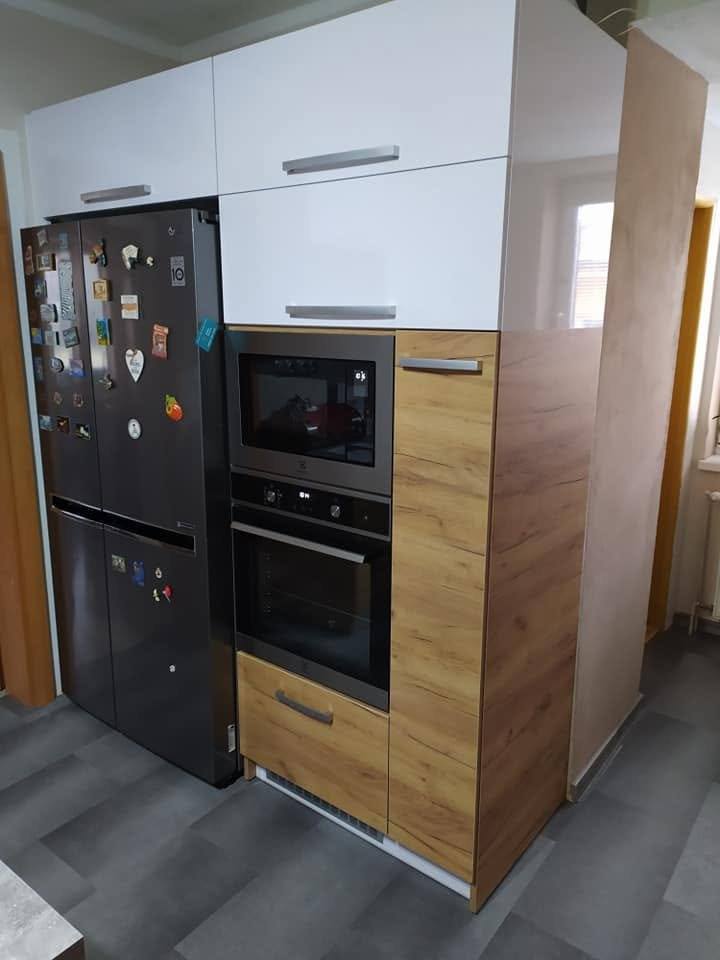 Zusammenspiel aus Eichendekor und weißem Hochglanz mit Backrohr und großem Kühlschrank.