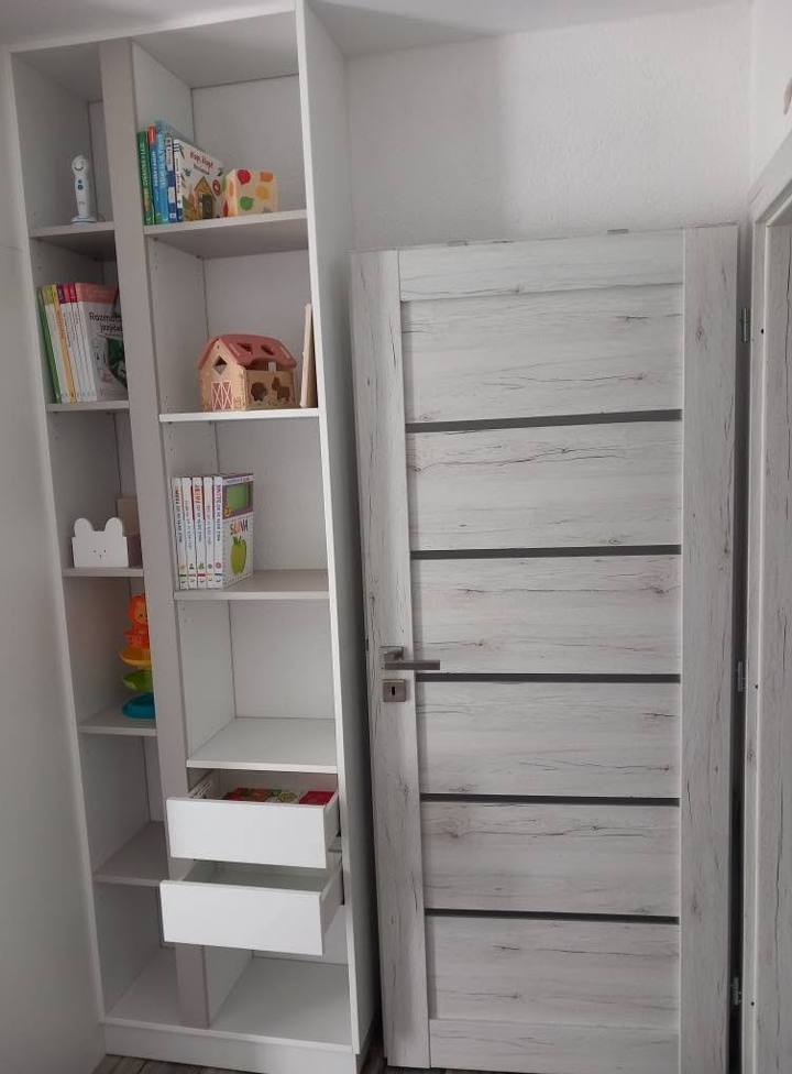 Weißes Regal mit Spielzeug und herausgezogenen Laden neben der Tür