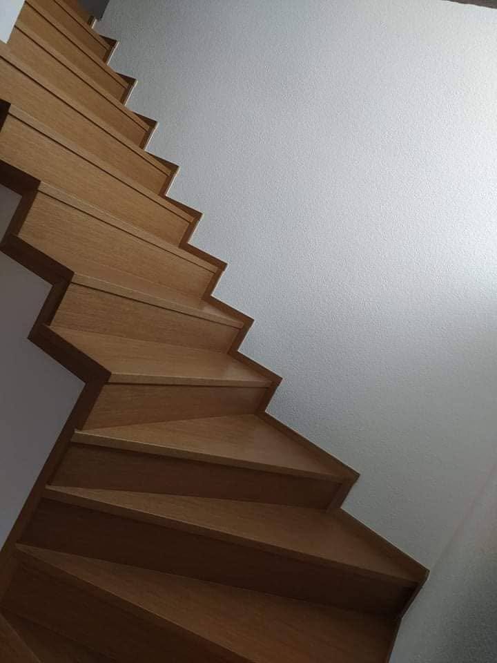 Gewendelte Stiege in heller Eiche entlang der fensterlosen weißen Wand