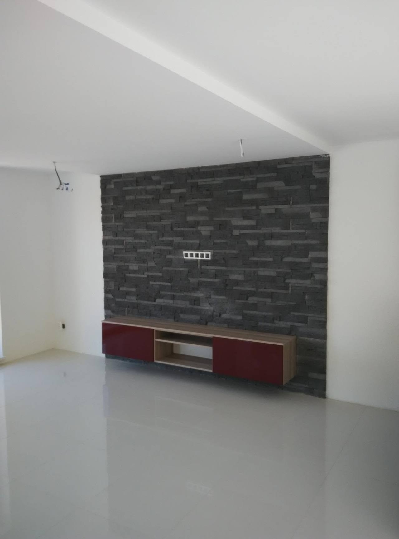 Schwebendes bordeauxfarbenes TV-Möbel an der dunklen Steinwand